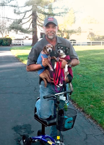 man on a knee scooter holding two puppies