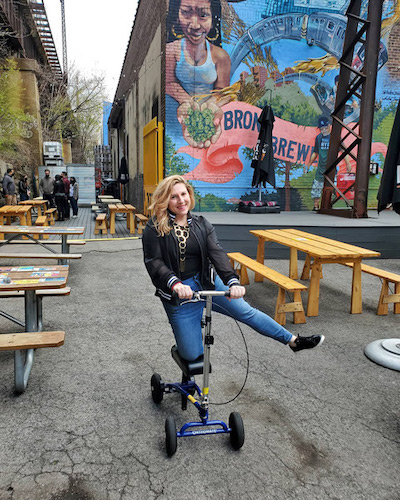 woman outdoors at a brewery riding an all-terrain knee scooter