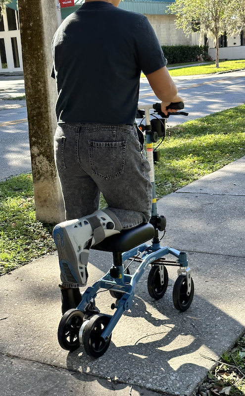 woman riding a knee scooter on sidewalk