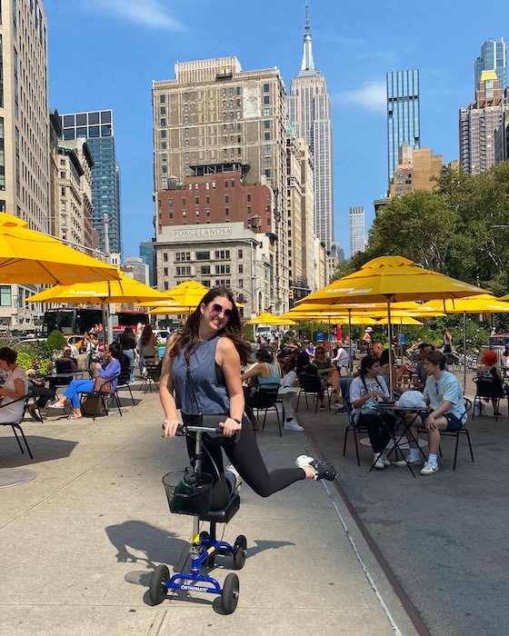 woman riding a knee scooter posing in front of the Empire State building