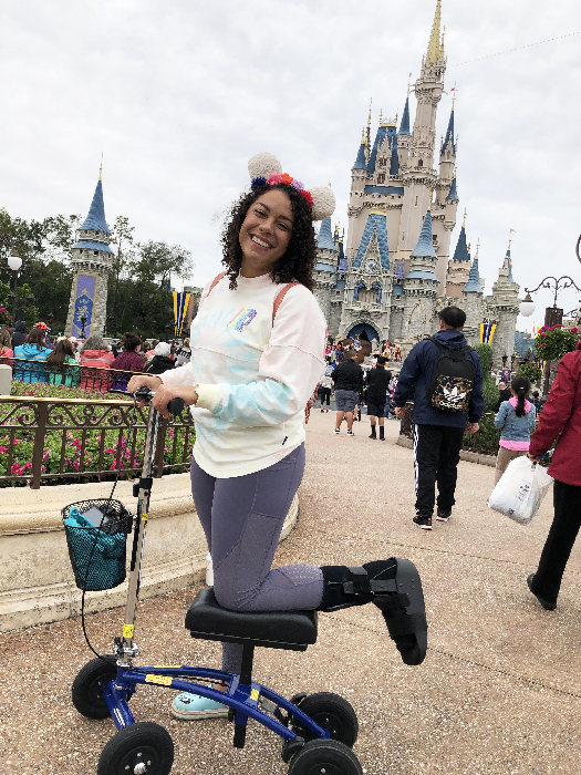 smiling woman riding a knee scooter with cinderella castle in the background