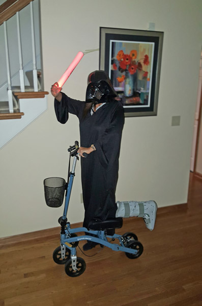 person with a darth vader costume, holding a red light saber. He is riding a knee scooter