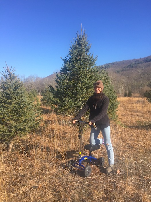woman on a knee scooter posing next to a christmas tree outdoors
