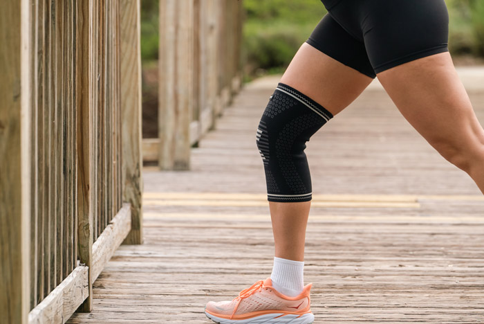 female with a knee compression sleeve stretching her leg