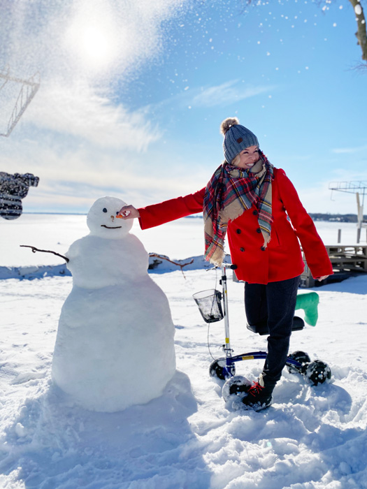 lady in the snow putting a nose onto a snowman