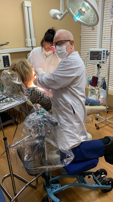  Ensuring his safety and stability, a dentist confidently performs his duties in the dental clinic while relying on a knee scooter for support.