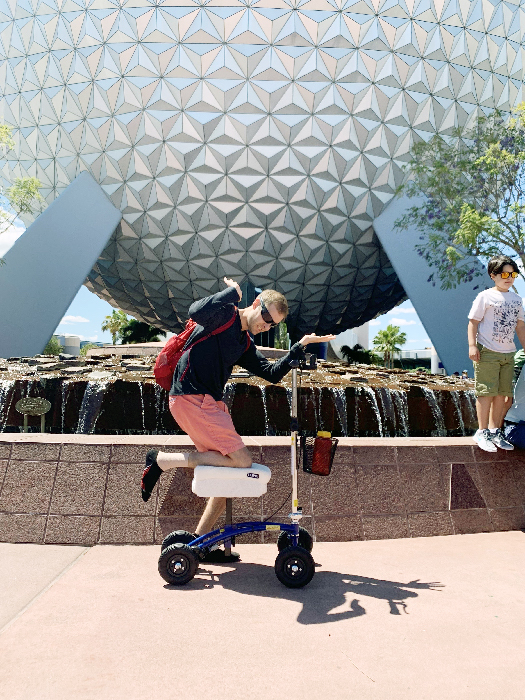 Man posing with a knee scooter in front of Epcot ball