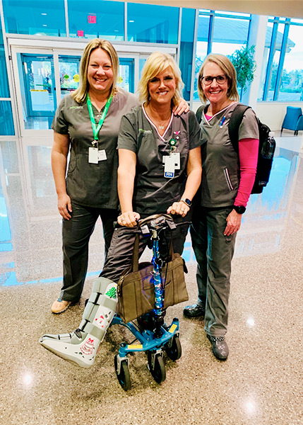 three nurses, one of them showing her boot and knee scooter