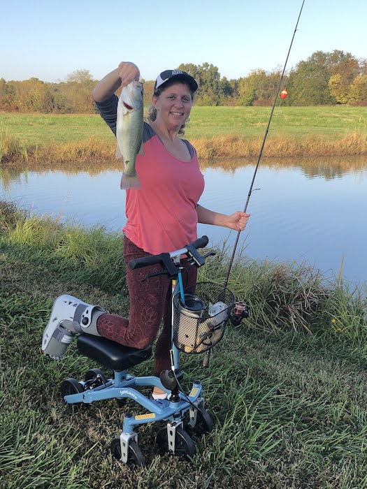 woman on a knee scooter holding a fish near a lake