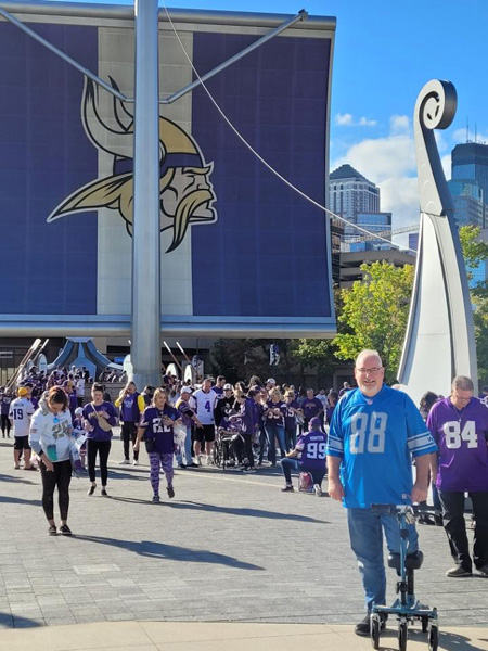 man posing with his knee scooter in front of a football stadium